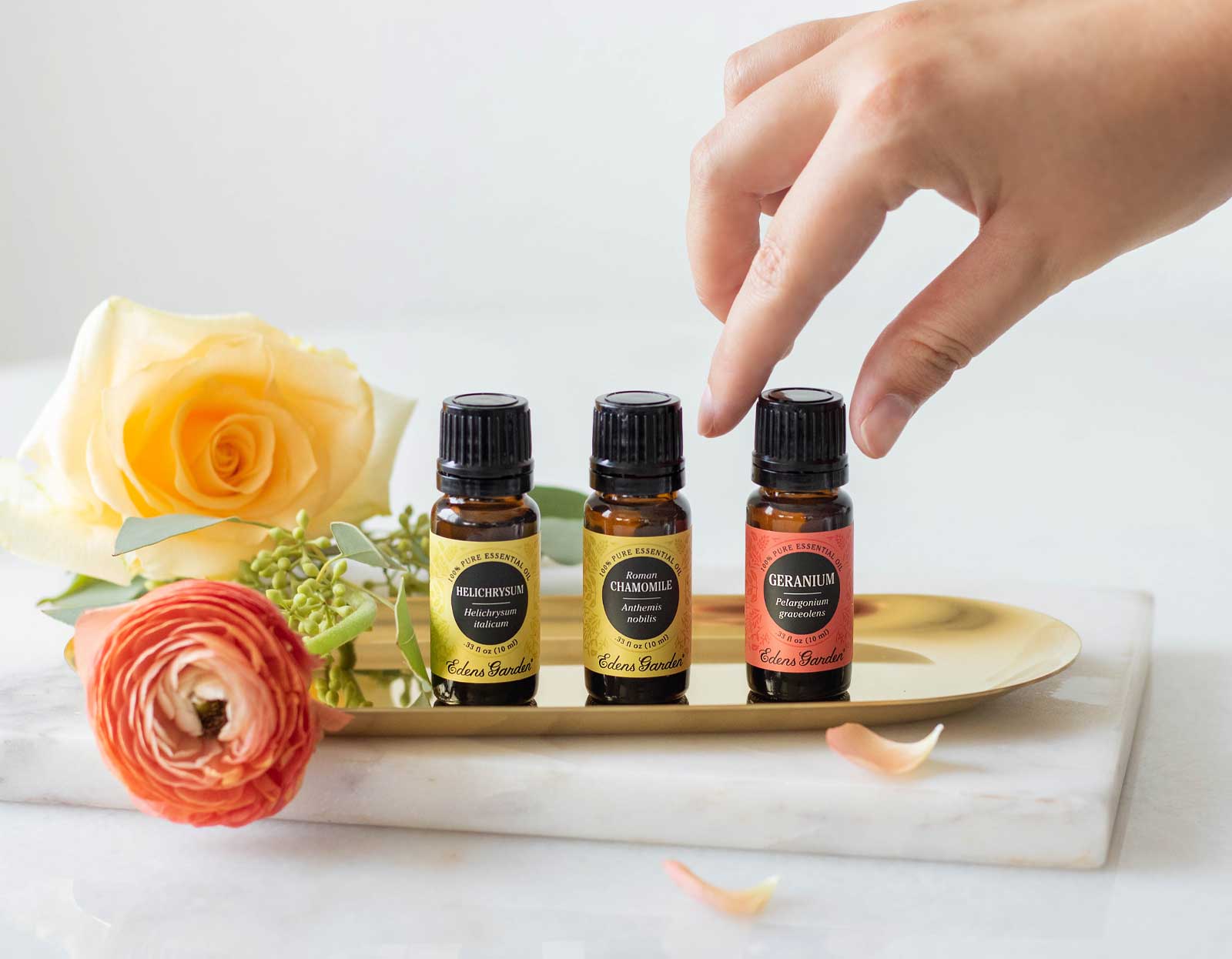 Three amber bottles of essential oils with rose petals and a rose bloom