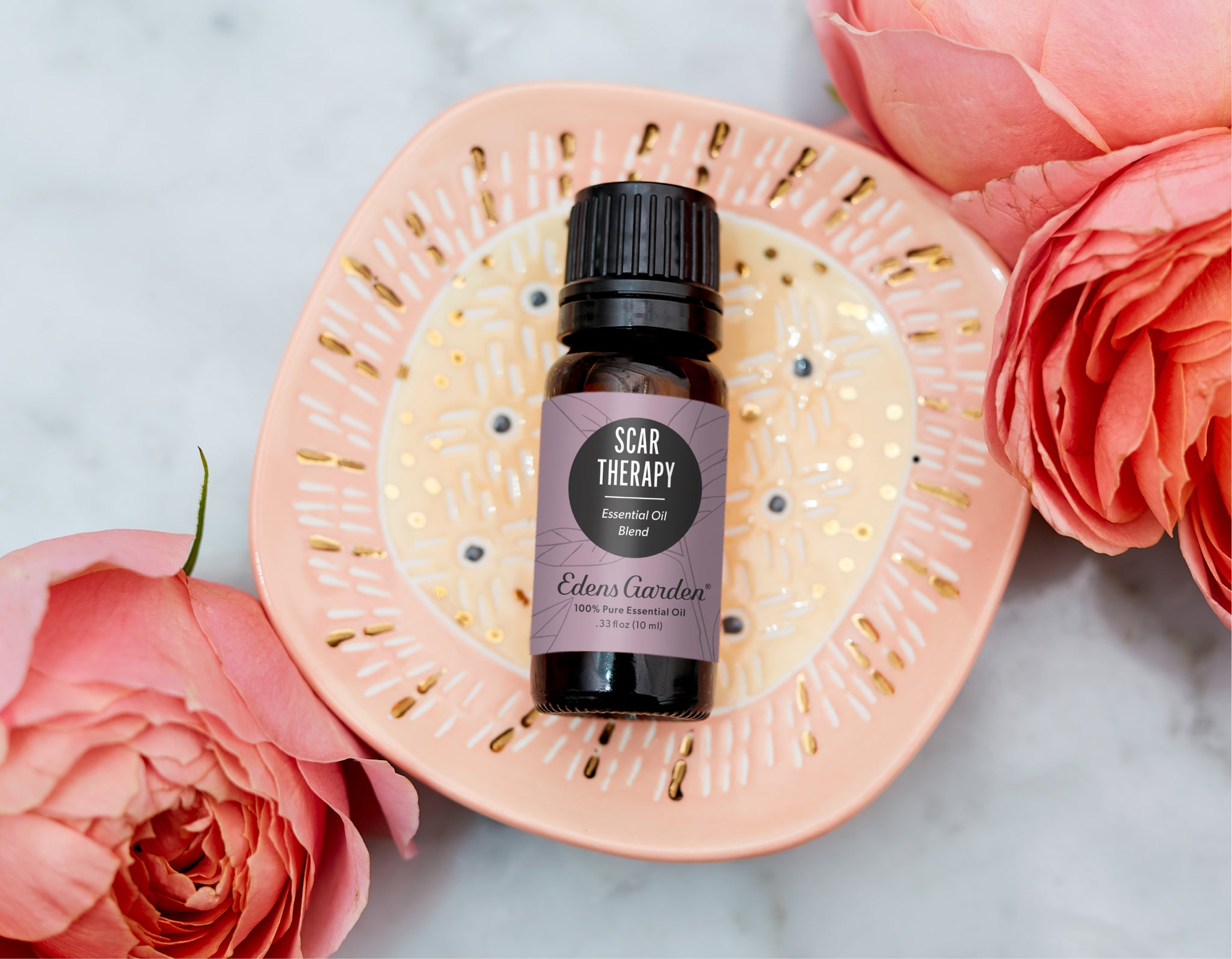 Edens Garden 'Scar Therapy' essential oil bottle on a pale pink plate surrounded by roses, suggesting scar care and gentle skincare