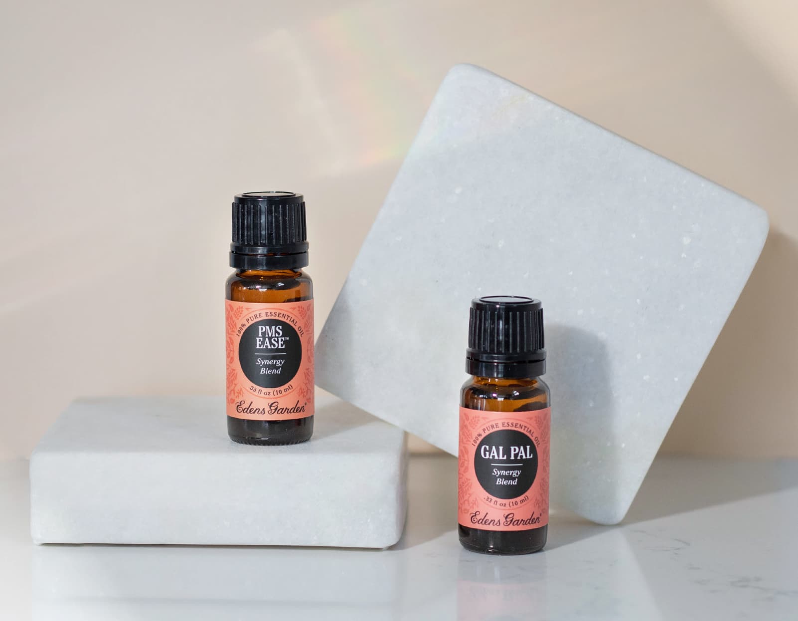 Two amber glass bottles of essential oil blends labeled PMS Ease and Gal Pal on a neutral background