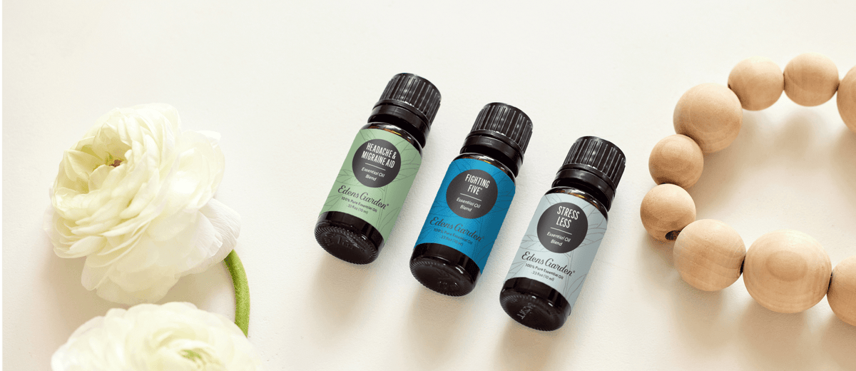 Three essential oil bottles with flowers and wooden beads beside them