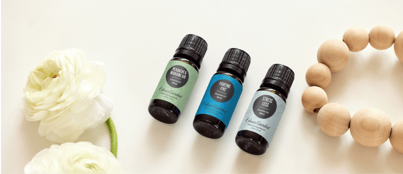 Three essential oil bottles with flowers and wooden beads beside them