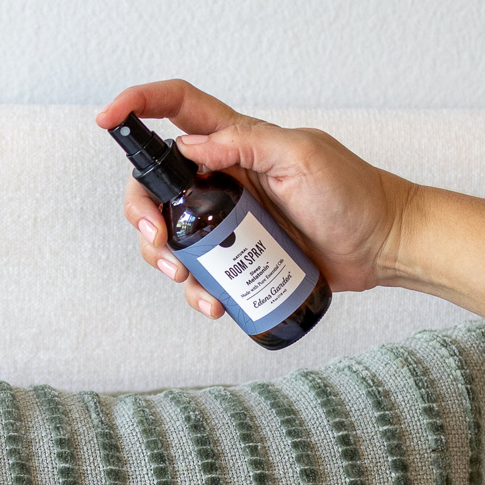 Hand holding a bottle of room spray with a label against a neutral background