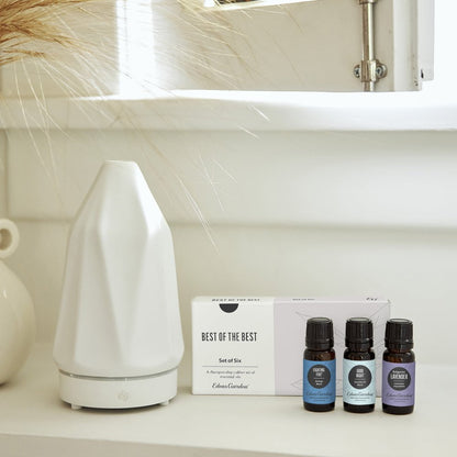 White diffuser and essential oil bottles on a shelf with a neutral background