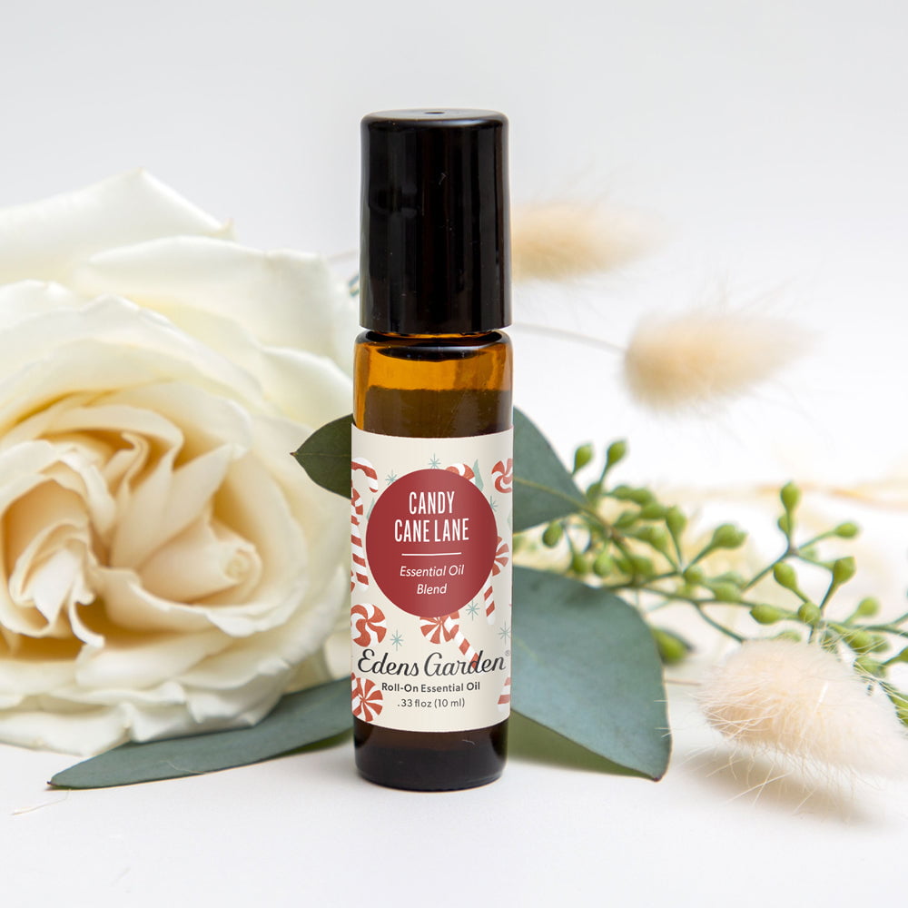 Roll-on essential oil bottle labeled 'Candy Cane Lane' by Edens Garden with white roses and greenery in the background.