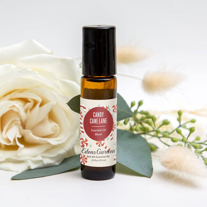 Roll-on essential oil bottle labeled 'Candy Cane Lane' by Edens Garden with white roses and greenery in the background.