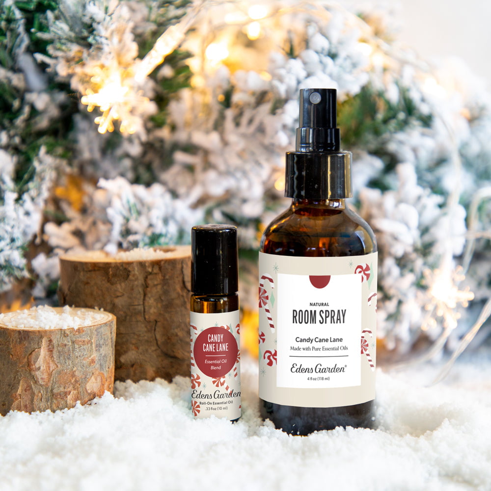 Two bottles of Edens Garden room spray and candy cane lane oil with a Christmas tree and lights in the background.