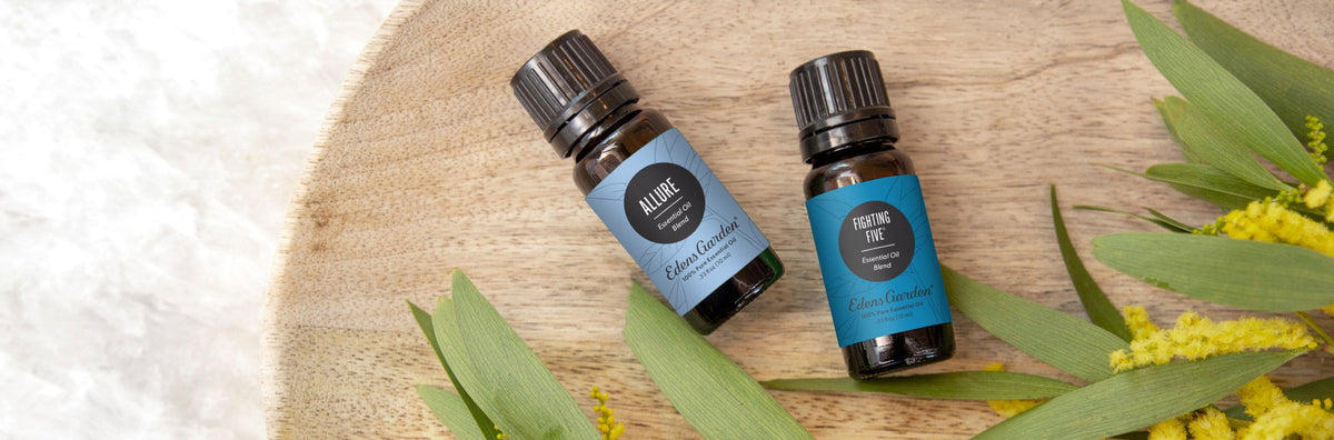 Two essential oil bottles on a wooden tray next to foliage and yellow flowers