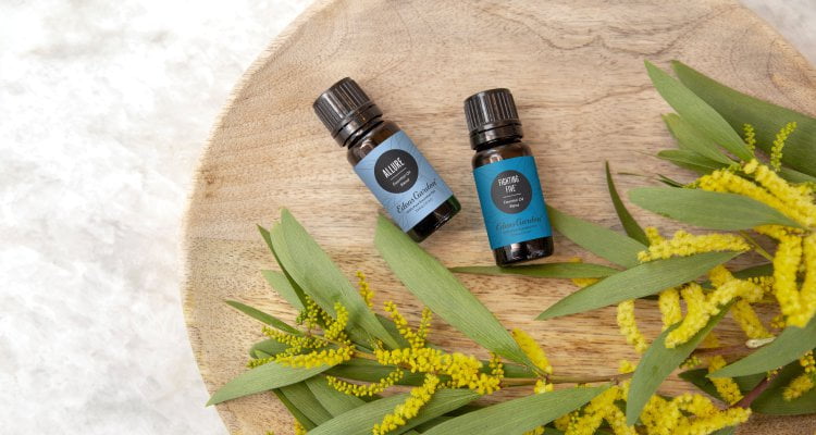 Two essential oil bottles on a wooden tray next to foliage and yellow flowers