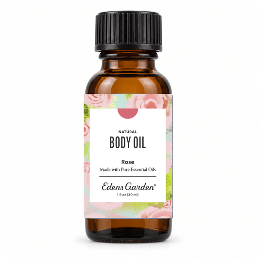 An amber glass bottle of Edens Garden Natural Body Oil in Rose, featuring a black ribbed cap and a white label with pink rose illustrations and green accents, set against a plain white background.