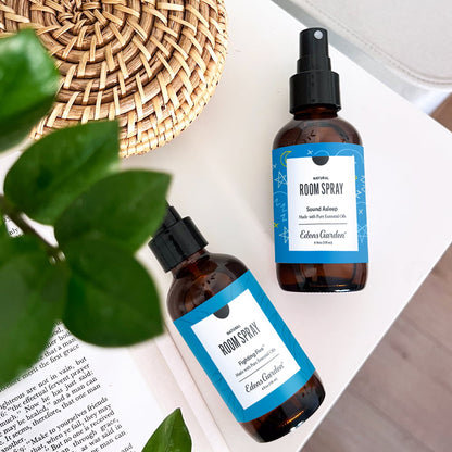 Two room spray bottles from Edens Garden pure aromatherapy with blue labels on a surface with green leaves.