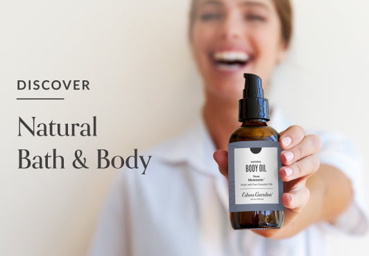 Edens Garden Natural Amber Glass Body Oil being displayed by a smiling woman with a white, blurred background. 