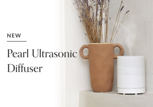 New Pearl Ultrasonic Diffuser by Edens Garden in use on a grey stone ledge next to a natural ceramic pot with lavender botanicals on a white background. 