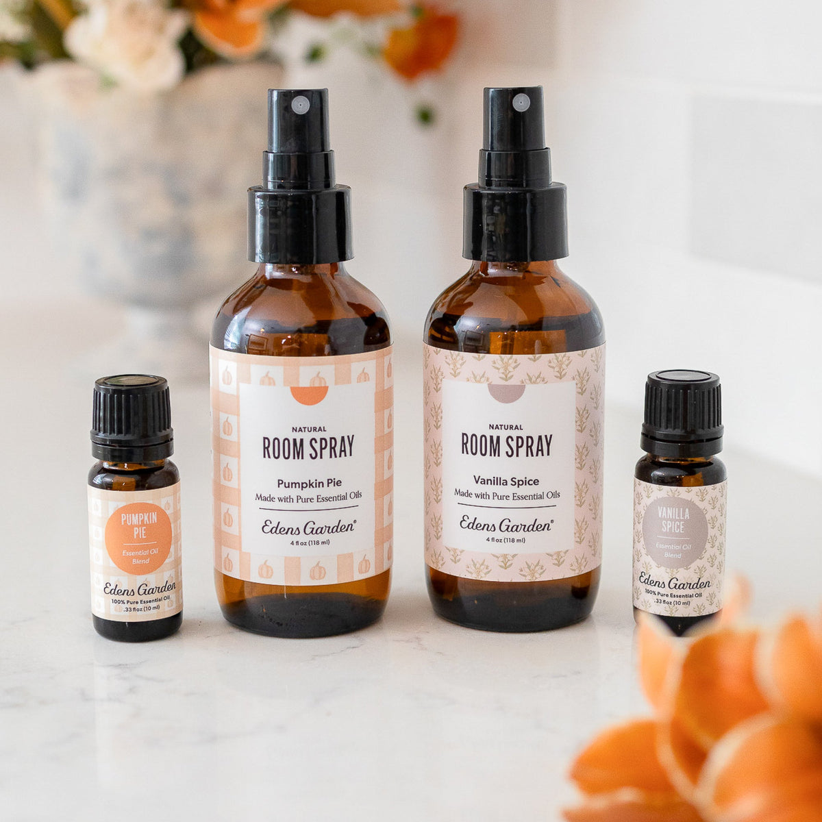 Set of room spray bottles and essential oils on a marble surface with floral decorations.