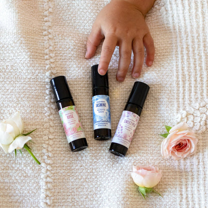 Three small perfume bottles with labels on a textured surface surrounded by flowers