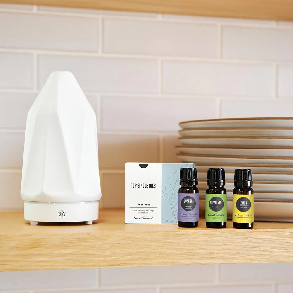 White diffuser on a wooden surface with essential oil bottles and packaging in the background.