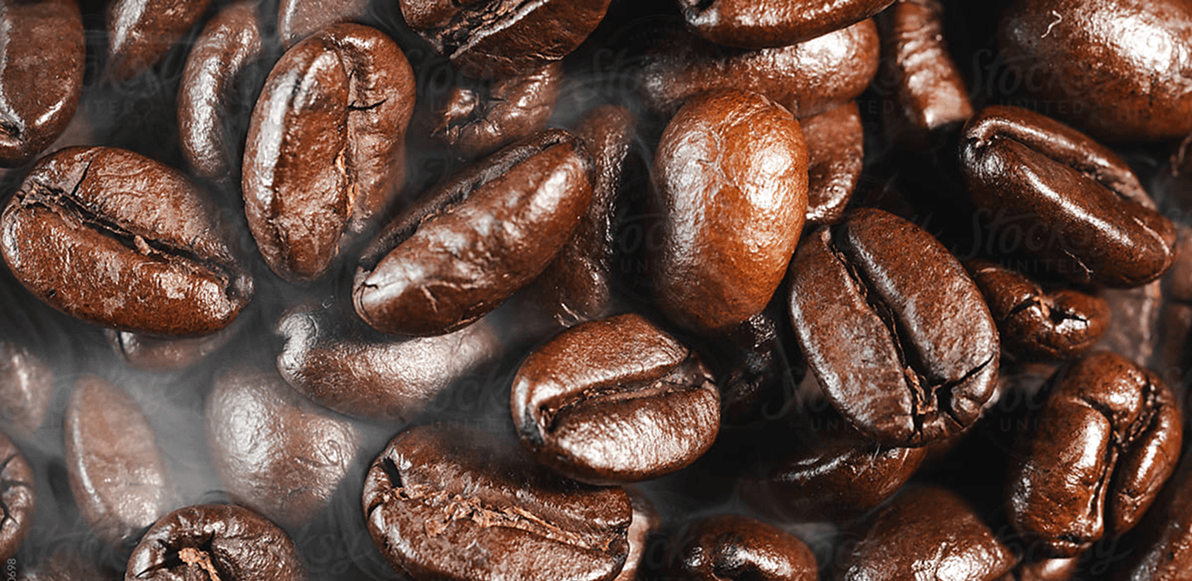 A close-up pile of glossy roasted coffee beans filling the frame, with visible steam or smoke around the edges.
