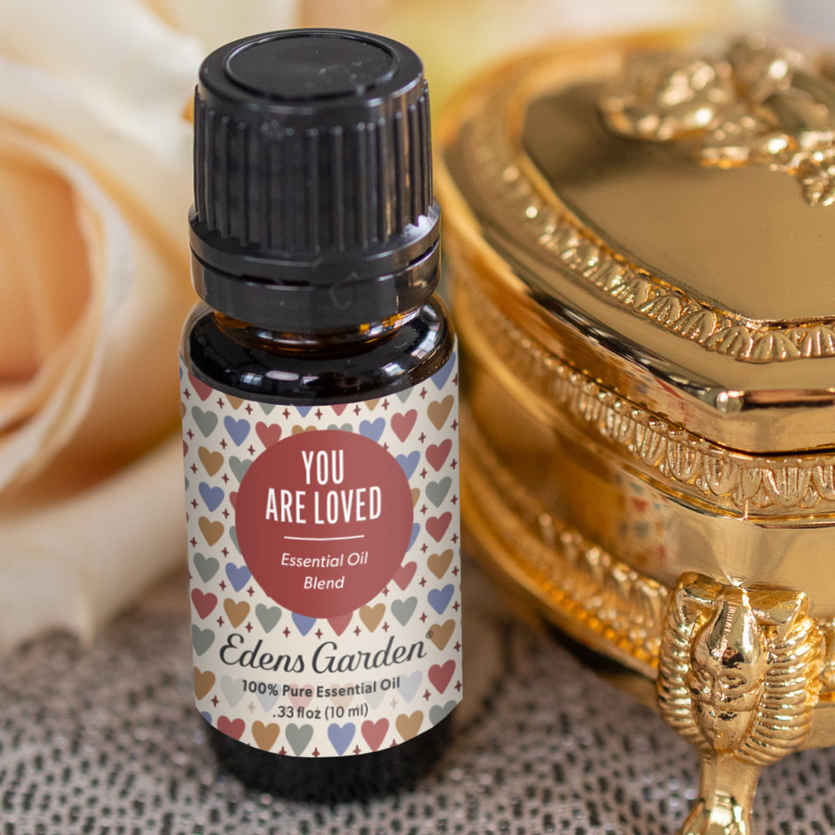 Edens Garden essential oil bottle with heart-patterned label next to a gold decorative box.