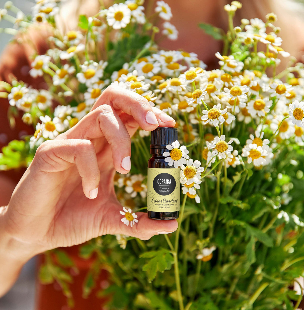 A woman holding up a bottle of essential oil with a bouquet of dainty white flowers