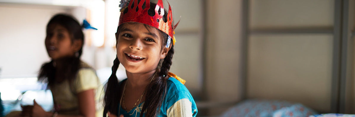 A little girl smiling and wearing a paper crown