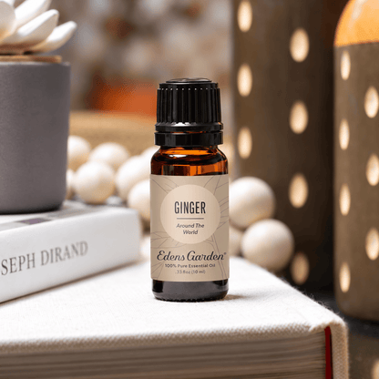 Edens Garden Ginger Around The World 10 ml amber bottle on a book beside a flower diffuser and patterned vases.